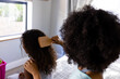 © Wavebreak Media - Rear view of biracial mother brushing her daughter's hair and sitting on bed in bedroom