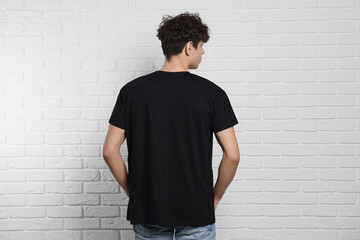 Wall Mural - Man wearing black t-shirt near white brick wall, back view. Mockup for design