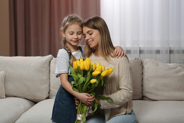 Wall Mural - Little daughter congratulating mom with bouquet of yellow tulips at home. Happy Mother's Day