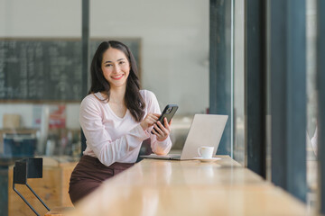 Beautiful asian businesswoman in the cafe, using smartphone and smiling.