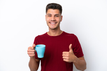 Wall Mural - Young caucasian man holding cup of coffee isolated on white background with thumbs up because something good has happened