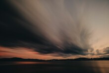 Long Exposure Shot Of The Gray Clouds Above A Calm Sea With The Sunset In The Background