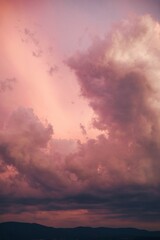 Canvas Print - Vertical shot of the big white clouds in the pink sunset sky with hill silhouettes underneath