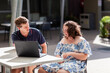 © Austockphoto - Adult and teenager talking together at outdoor café with laptop open