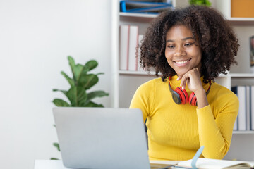 American teenage woman sitting in white room with laptop, she is a student studying online with laptop at home, university student studying online, online web education concept.