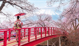 Fototapeta  - Woman traveller with a red umbrella and walking over the bridge with Fuji mountain and Sakura flower background