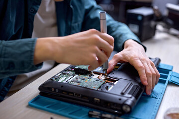 cropped professional IT specialist replacing details in computer repair workshop, hardware upgrading. A real case of service assistance. unrecognizable male sit at work place repairing old laptop