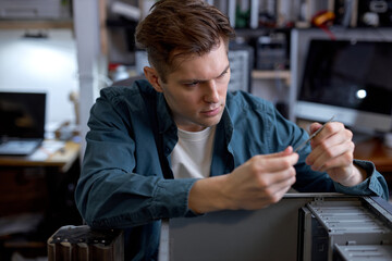 Wall Mural - Serious caucasian man disassembles broken computer. Computer service and repair concept. Computer disassembling in repair shop, workshop. Electronic development by professional technician