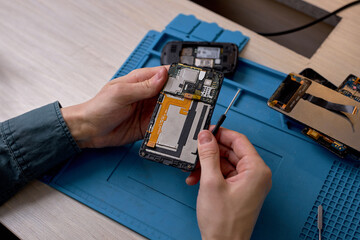 Wall Mural - smartphone technician checking a phone's components after disassembling it, Hand technician repairing broken mobile phone with tool, close-up photo focus on hands