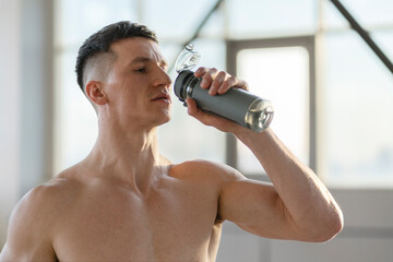 Wall Mural - Attractive fit man drinking water after training indoors. Healthy lifestyle training in gym