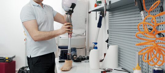 Crop unrecognizable craftsman adjusting and bending modern prosthetic leg at knee section at workbench in manufacturing factory