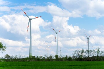 Wind turbines on a green hill against the blue sky with fluffy clouds