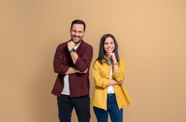 Wall Mural - Portrait of cheerful attractive boyfriend and girlfriend dressed in casuals looking at camera. Smiling young couple touching chins and posing happily on isolated beige background