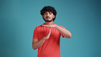 indian man with beard wearing coral t-shirt isolated on a blue studio background doing time out gesture with hands, frustrated and serious face