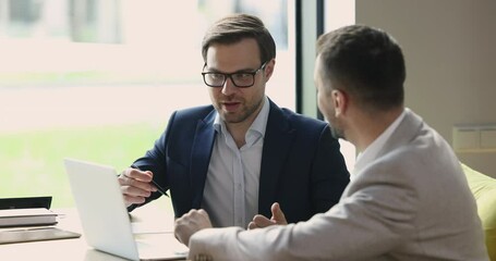 Serious confident business man telling about online project to partner, investor, speaking at open laptop. Mentor explaining listening intern work task. Manager, developer presenting software, app