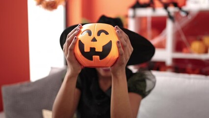 Sticker - African american woman wearing witch costume holding halloween pumpkin basket at home