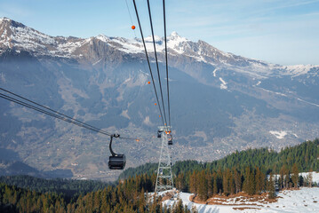 Wall Mural - Gondola lift moving on cables over pine trees growing in forest with beautiful view of Bernese mountains and sky in background at Jungfrau, Switzerland, winter holiday and nature concept