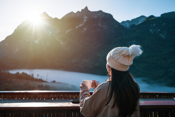 Young woman traveler with a cup of coffee looking beautiful mountains view in the morning