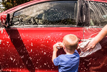 Toddler Boy Washing Red Car With Help Of Dad
