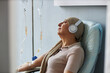 © Seventyfour - Side view portrait of senior woman listening to music during chemotherapy treatment, copy space