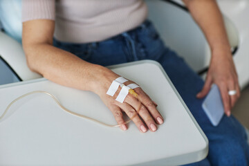 Closeup of female hand with IV drip during treatment session in clinic, copy space