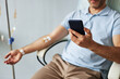 © Seventyfour - Closeup of unrecognizable man using smartphone during IV drip treatment, copy space