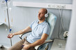 © Seventyfour - High angle portrait of adult man wearing headphones and relaxing during IV drip treatment in clinic