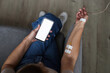 © Seventyfour - Top view closeup of unrecognizable man using smartphone with white screen mockup during IV drip treatment, copy space