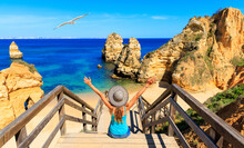 Happy woman tourist sitting on footbridge to beautiful beach praia do camilo,  ponta da piedade- Algarve beach,  tourism in Portugal