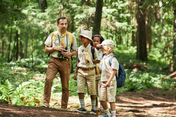 Full length view at diverse group of scouts hiking in forest with adult leader, copy space