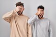 © Krakenimages.com - Young homosexual couple standing over white background peeking in shock covering face and eyes with hand, looking through fingers with embarrassed expression.