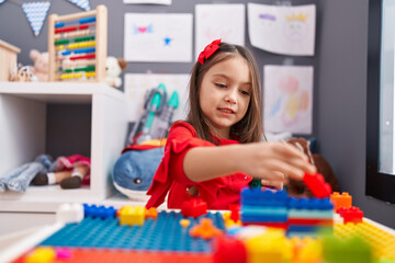 Wall Mural - Adorable hispanic girl playing with construction blocks sitting on table at kindergarten