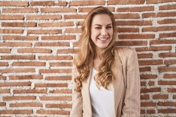 Wall Mural - Beautiful blonde woman standing over bricks wall winking looking at the camera with sexy expression, cheerful and happy face.