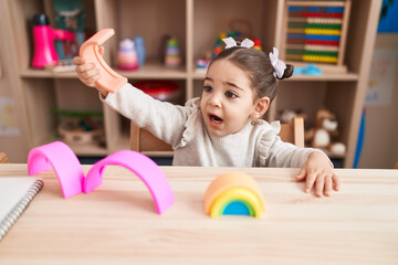 Wall Mural - Adorable hispanic girl playing with construction blocks sitting on table at kindergarten