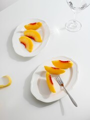 Wall Mural - Flat lay of cut peach slices on white plates with a minimalistic table set