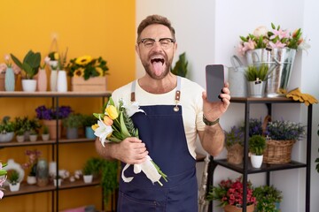 Sticker - Middle age man with beard working at florist shop showing smartphone screen sticking tongue out happy with funny expression.