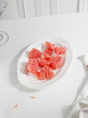 Canvas Print - Vertical shot of a plate of red pomelo pieces on a white table