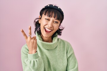 Poster - Young beautiful woman standing over pink background smiling with happy face winking at the camera doing victory sign with fingers. number two.