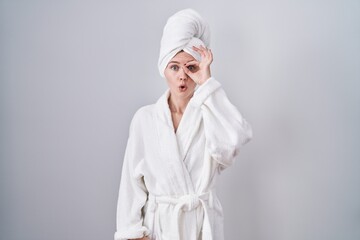 Poster - Blonde caucasian woman wearing bathrobe doing ok gesture shocked with surprised face, eye looking through fingers. unbelieving expression.