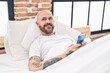 © Krakenimages.com - Young bald man using smartphone lying on bed at bedroom