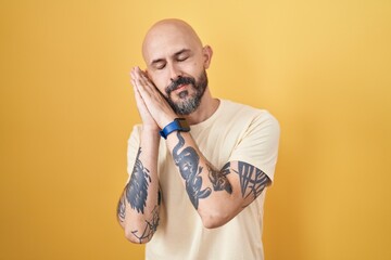 Wall Mural - Hispanic man with tattoos standing over yellow background sleeping tired dreaming and posing with hands together while smiling with closed eyes.