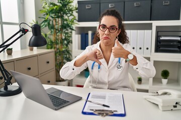 Canvas Print - Young hispanic woman wearing doctor uniform and stethoscope doing thumbs up and down, disagreement and agreement expression. crazy conflict