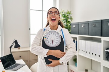 Sticker - Young hispanic woman working at dietitian clinic angry and mad screaming frustrated and furious, shouting with anger looking up.