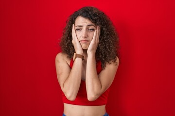 Sticker - Hispanic woman with curly hair standing over red background tired hands covering face, depression and sadness, upset and irritated for problem