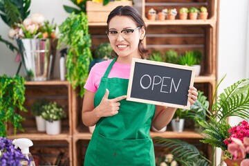 Poster - Hispanic young woman working at florist holding open sign smiling happy pointing with hand and finger