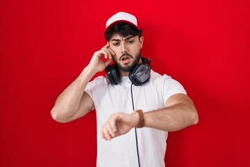 Canvas Print - Hispanic man with beard wearing gamer hat and headphones looking at the watch time worried, afraid of getting late