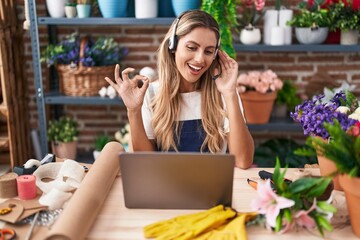 Canvas Print - Young blonde woman working at florist shop doing video call doing ok sign with fingers, smiling friendly gesturing excellent symbol