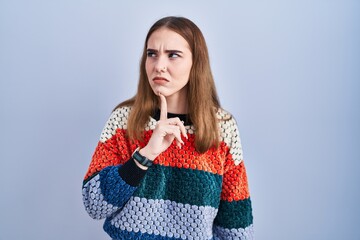 Wall Mural - Young hispanic girl standing over blue background thinking concentrated about doubt with finger on chin and looking up wondering