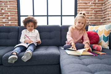 Sticker - Adorable boy and girl students sitting on sofa drawing on notebook at home