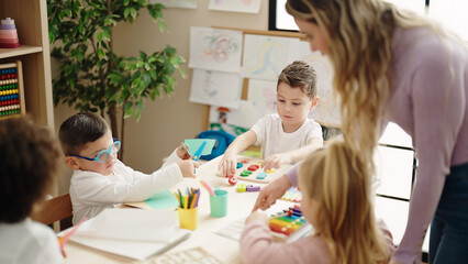 Poster - Woman and group of kids having lesson sitting on table at kindergarten